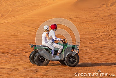 Quad Biking Dubai Adventure Tour â€“ Young copule of tourists having fun on Quad Bike Riding in dunes of Dubai Stock Photo